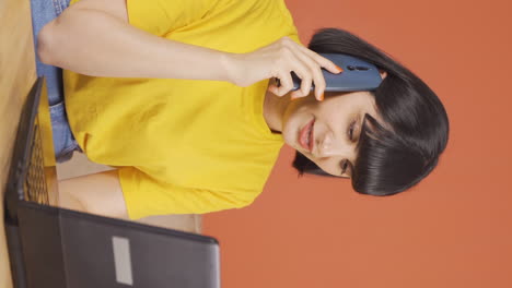 Vertical-video-of-Young-woman-using-laptop-nervously-talking-on-the-phone.